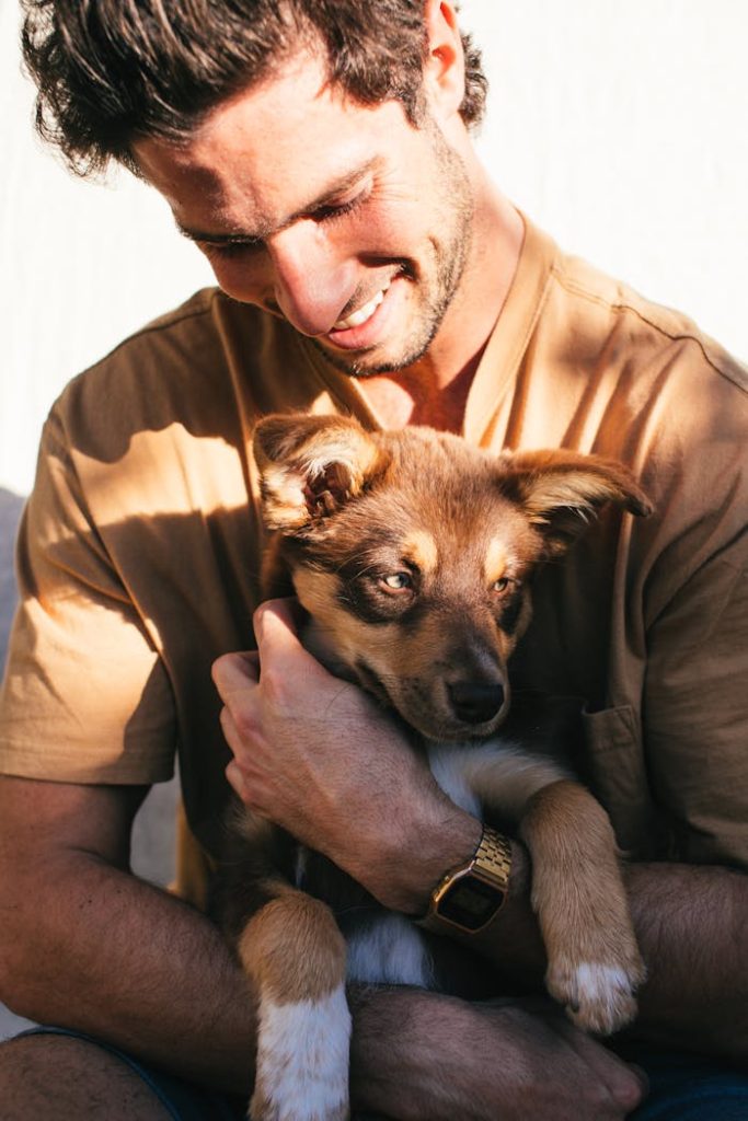 pexels photo 5490235 Smiling man embraces a cute puppy outside on a sunny day, expressing joy and companionship.